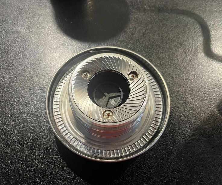 A stainless steel coffee grinder burr on a black counter.