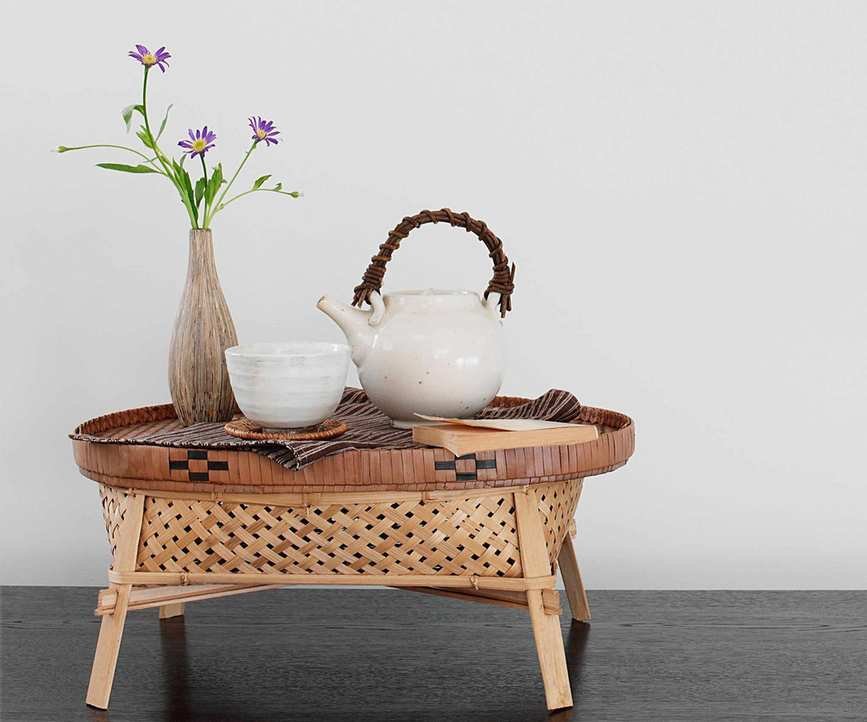 Decorative white teapot with leather woven handle and ribbed mug, sat on top of a wicker storage tray with legs