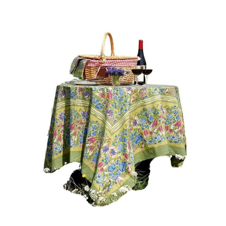 A green tablecloth with a blue and red floral pattern on it, and a basket and wine glasses on top of it