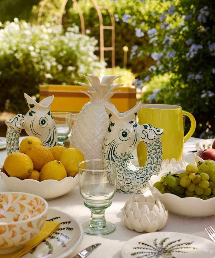 Mediterranean themed outdoor dinner party table with fish jugs, a pineapple centerpiece, bowl of lemons and palm tree plates