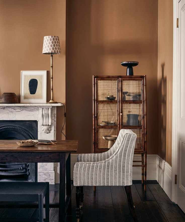 Dining room painted in a dark ochre shade with natural textures and a rustic cabinet