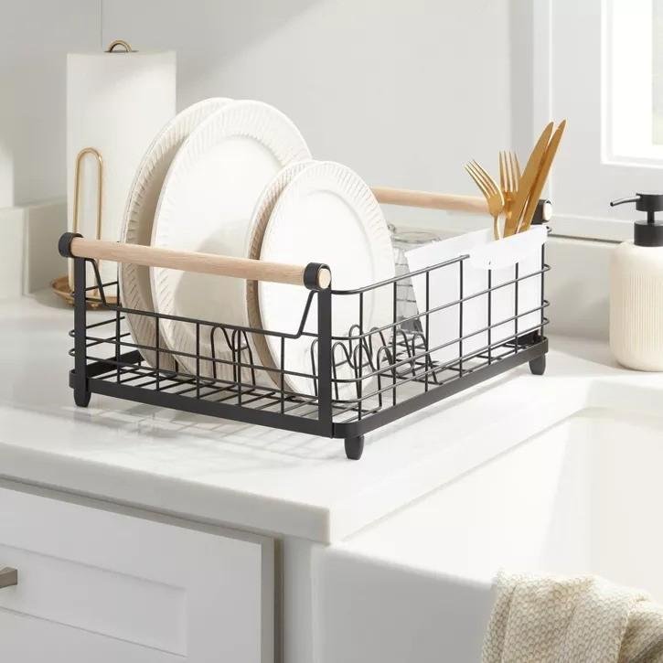 A black metal dish rack with wooden handles, stacked with white dinner plates
