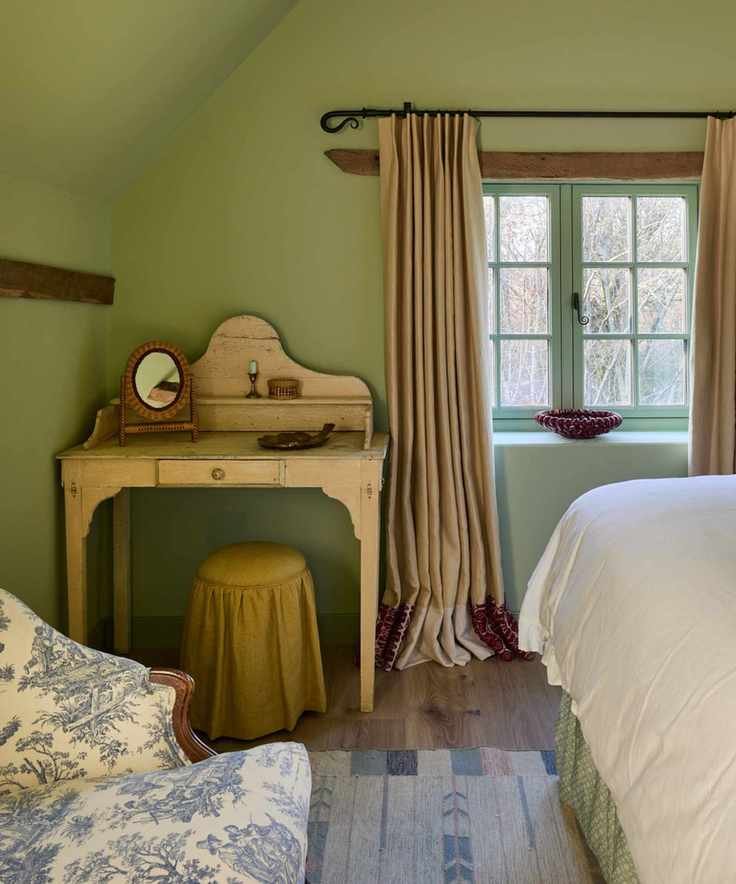 vintage country bedroom with oak beams painted in a soft green with a vintage dressing table and small upholstered ochre stool