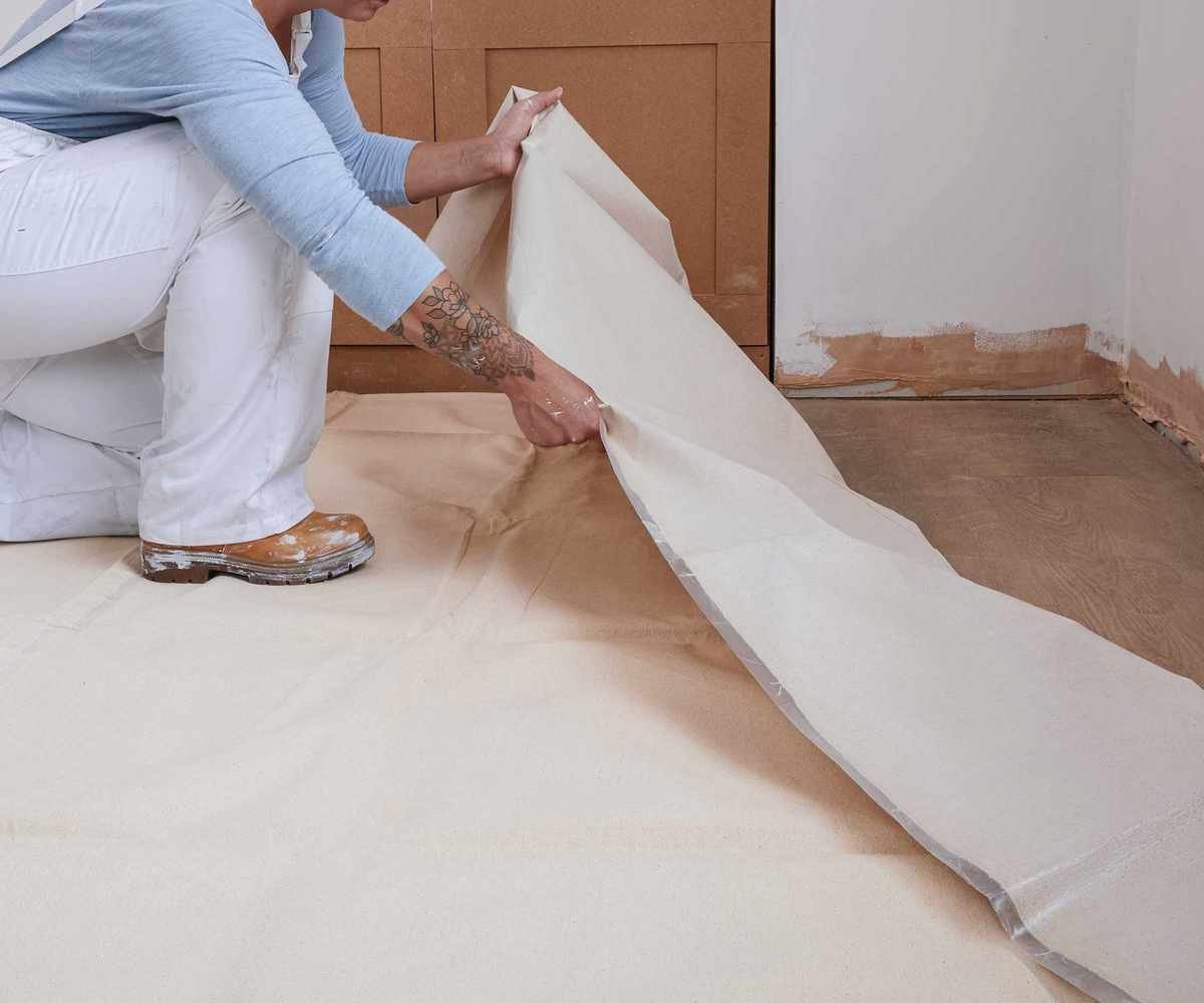 woman in white overalls laying down a dustsheet to decorate
