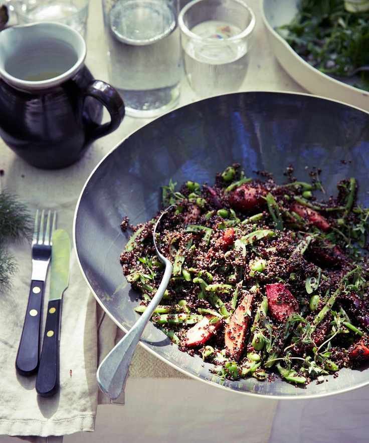 Black quinoa and beet salad in a large grey bowl on a table with knife, fork, jug, water glass, and linen napkin