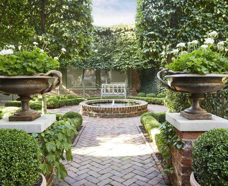 A garden with circular water fountain at the centre of symmetrical formal garden layout, with classical style urns