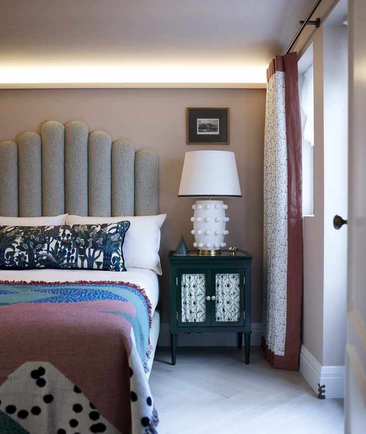 Bedroom with double bed with upholstered headboard, bedside table and lamp, neutral walls and floor