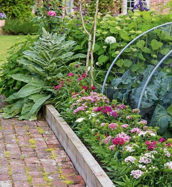 A flower bed with pink flowers and a wooden border next to a stone patio