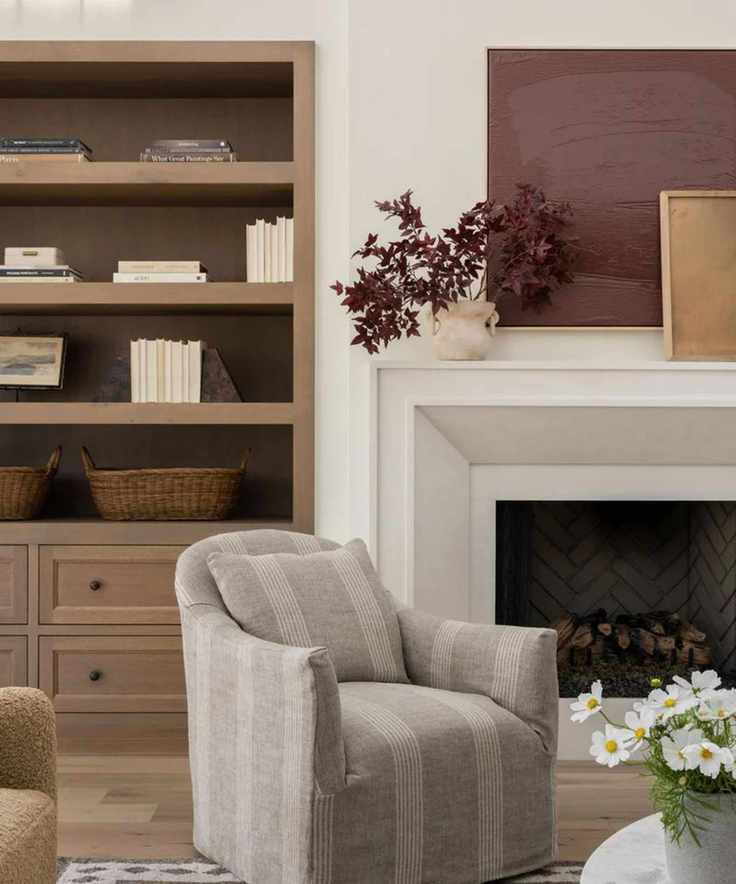 Neutral living room with rust colored art and dark red faux foliage in a vase on the mantel