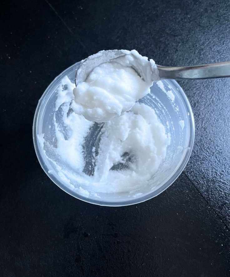A baking soda paste in a round plastic container, sliding off a metal teaspoon