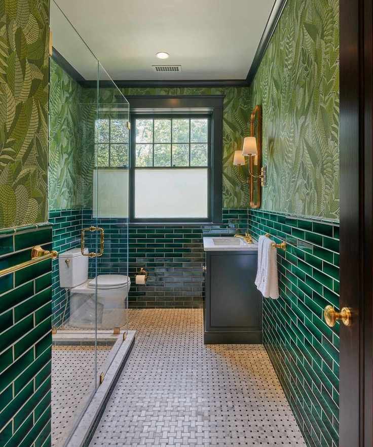 A small green bathroom with dark green subway tiles and leaf-themed wallpaper.