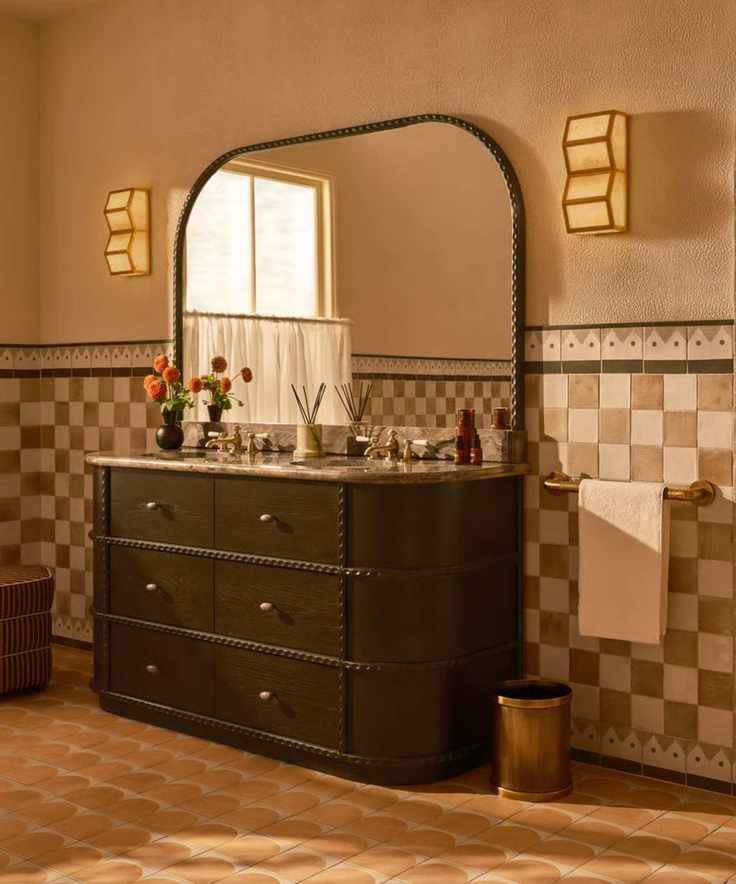 A warm neutral bathroom with white and beige checkerboard wall tiles, a dark wood vanity, and a curved dark wood vanity mirror