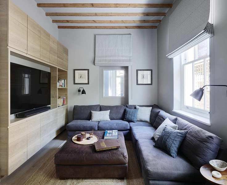 Living room showcasing a large gray L-shaped sofa, ottoman, built-in storage for the TV, wooden beams, gray walls, and framed artwork