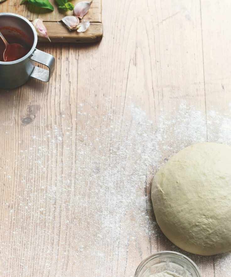 Ball of dough on a floured wooden surface alongside a jug of tomato sauce