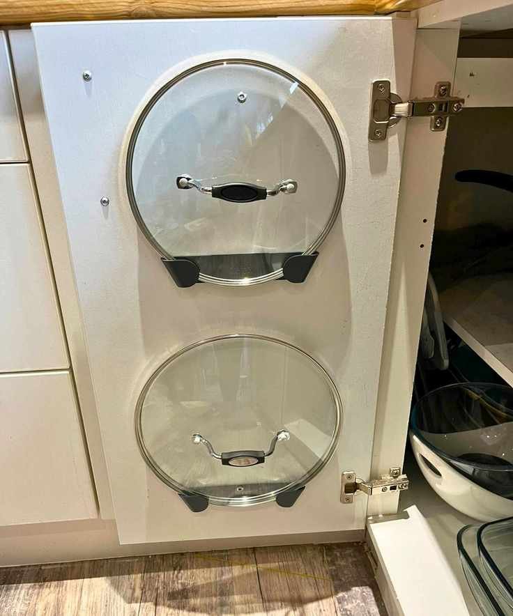 Two glass pan lids held on the inside of my kitchen cabinet door in the nifty adhesive Joseph Joseph pan lid holders