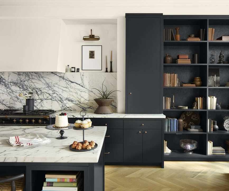 A kitchen with black cabinets, white walls, and a marble countertops and backsplash