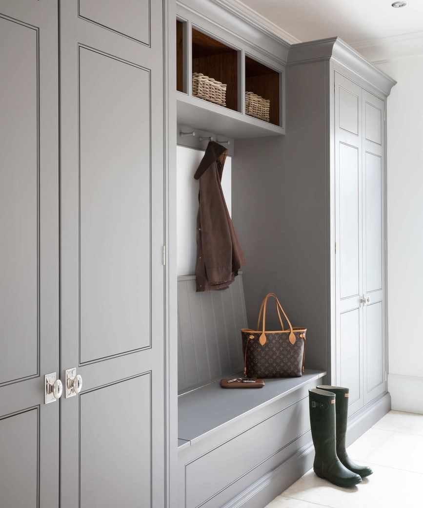 Contemporary gray boot room with floor to ceiling wooden storage cabinets, bench seating, boots on floor, coat hooks, wicker storage baskets
