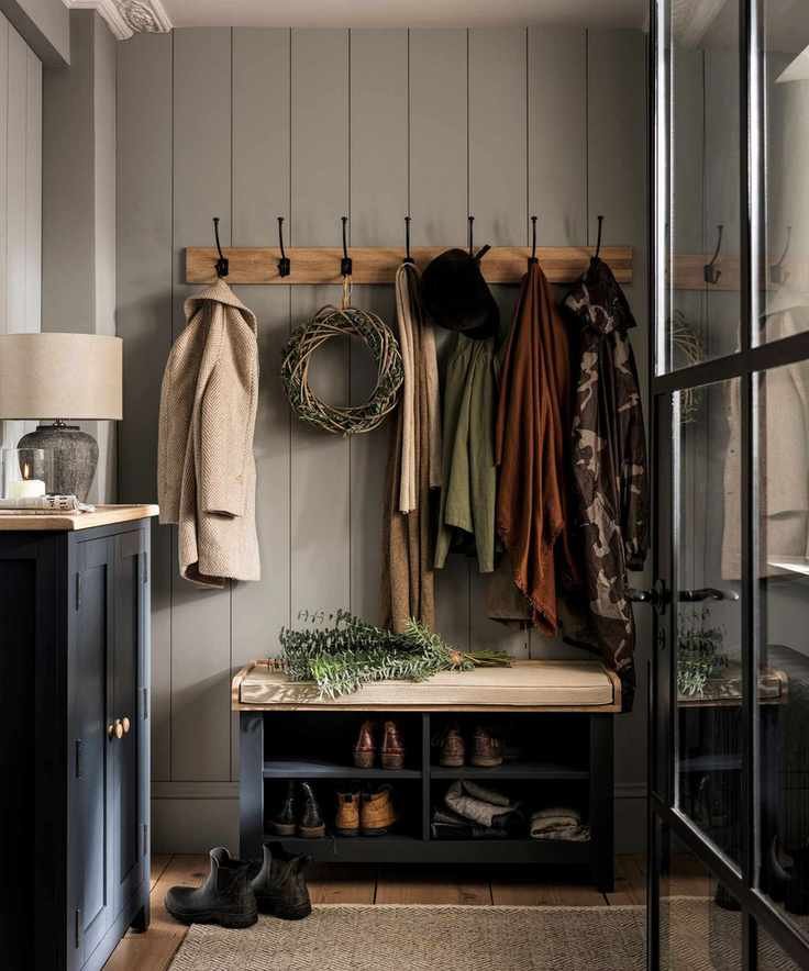 A rustic entryway with wall mounted coat hooks above a blue painted shoe storage bench, topped with a cream cushion.