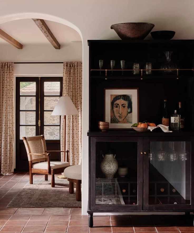 A white traditional kitchen with a dark wood freestanding cabinet featuring glass doors and a brass shelf rail