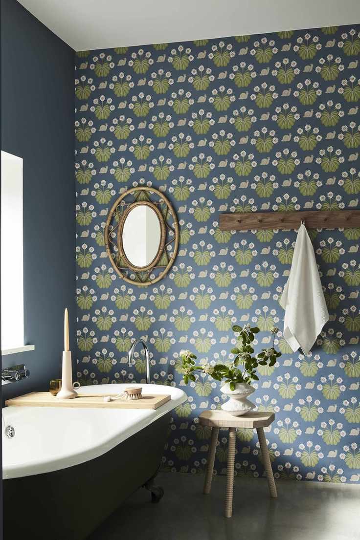 A blue bathroom with green and blue wallpaper with a rattan mirror and a peg rail