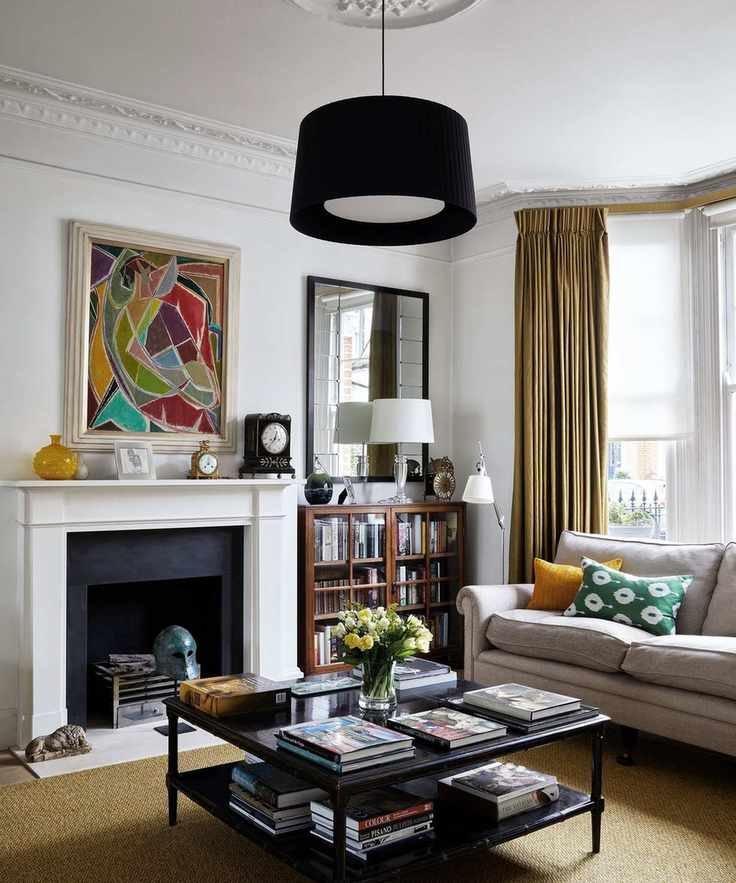 A living room with a white fireplace and a black ceiling light, gray sofa, black square coffee table, colorful artwork mounted above fireplace.