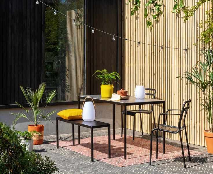 Black metal furniture with wood slatted fencing and string lights.