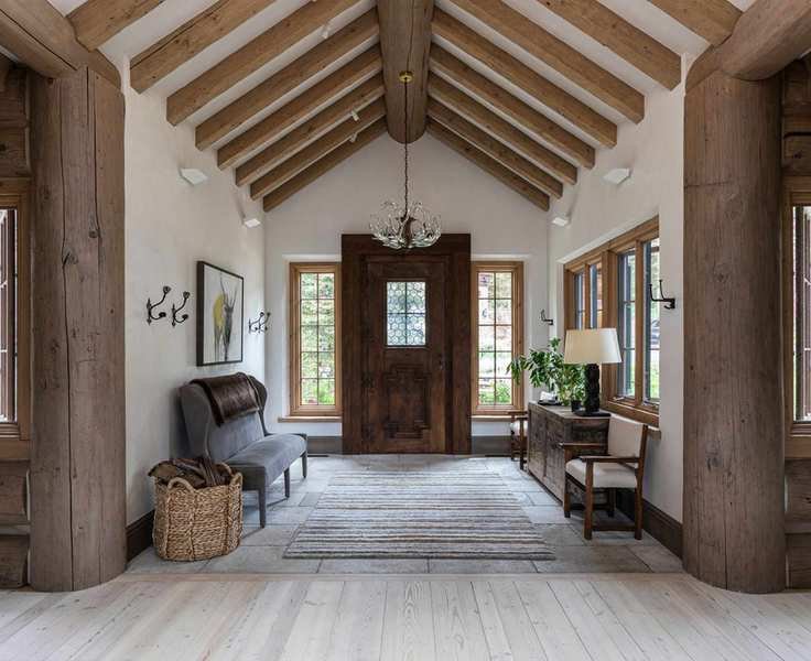Traditional interior with vaulted ceiling and wooden beams in entryway, featuring a large wooden front door and windows