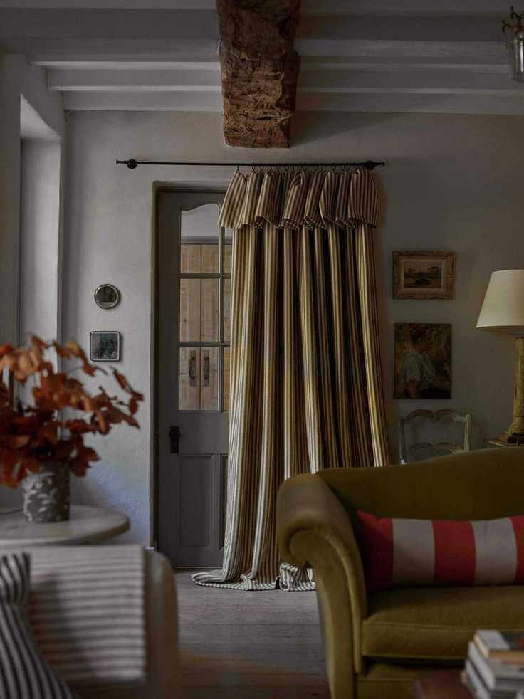 gray and green living room with striped curtain in front of door, green couch, stripe cushions, beams, paintings, fall stems in vase on side table
