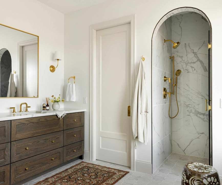A neutral guest bathroom with warm white walls, a dark wood vanity, and a marble shower nook