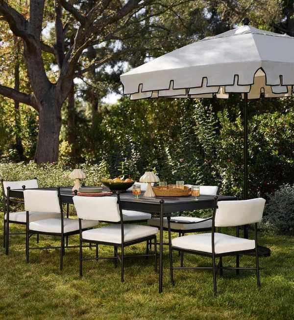 an outdoor dining area with a table, dining chairs with white cushions, and an umbrella