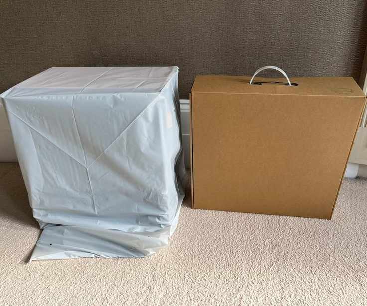 Two iRobot Roomba Combo j9+ boxes side by side, one cardboard and one with protective sleeve on cream carpet in front of brown wall in Alex's home