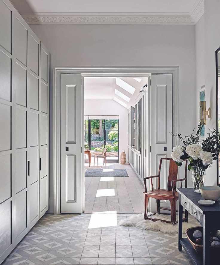 Hallway with grey and white tiled floor and built in cupboards on the left and console table and chairs to the right, view through to kitchen and garden.