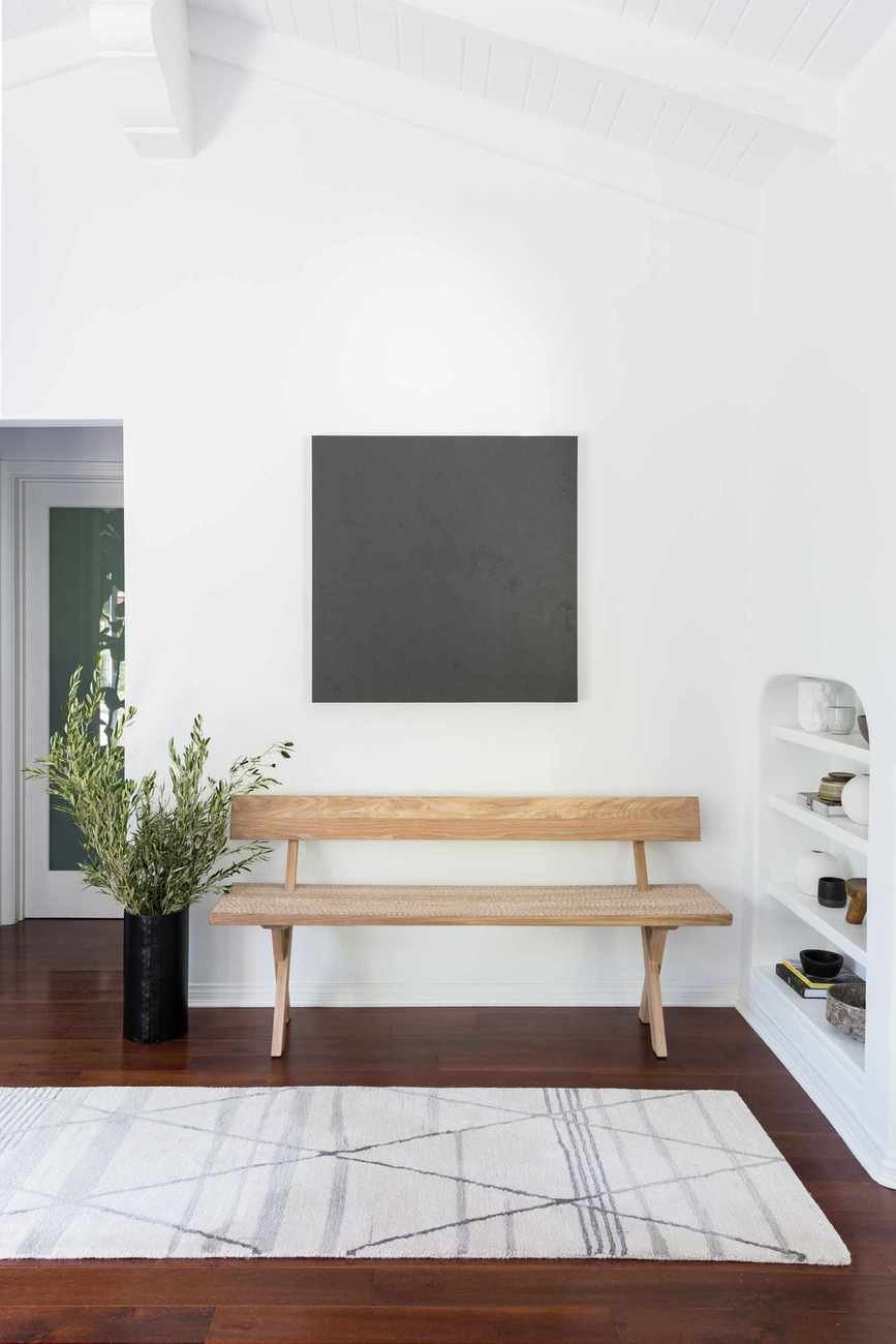 White entryway with rug, wood floor and wood bench