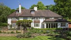 an exterior shot of a large English home in Surrey with a tiered garden surrounded by trees