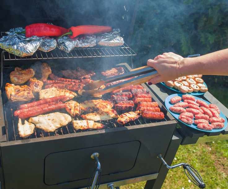 Grilling sausages, chicken breast, and peppers on an open grill