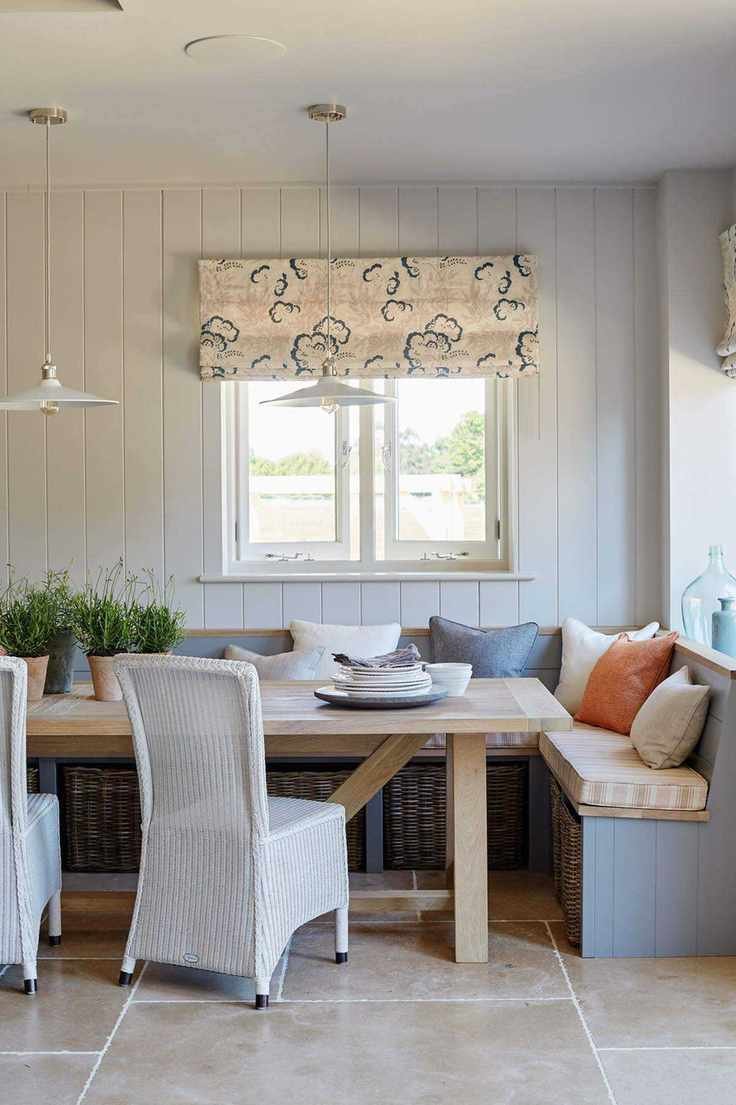 An example of small kitchen storage ideas showing a large wooden dining table with built-in banquette seating in front of a white paneled wall