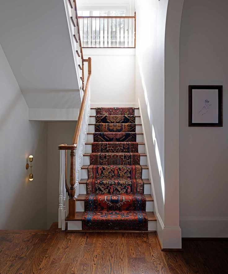 A white entryway with a staircase, patterned runner, and hardwood floors