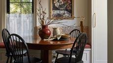 a cozy pattern layered dining nook with a banquette seat, small window and cafe curtain, wooden round table and black chairs