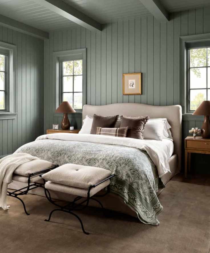 A serene blue-green bedroom featuring a neutral upholstered bed with wooden nightstands and two stylish ottomans at the foot