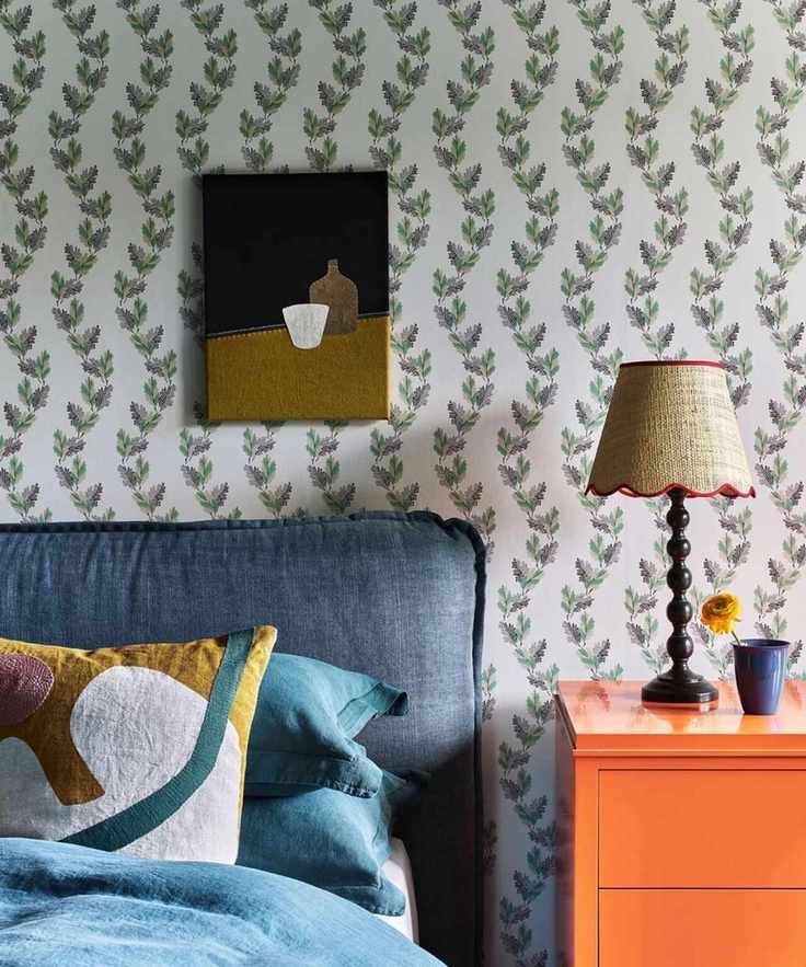 A blue fabric covered headboard with soft edges next to a bright orange nightstand