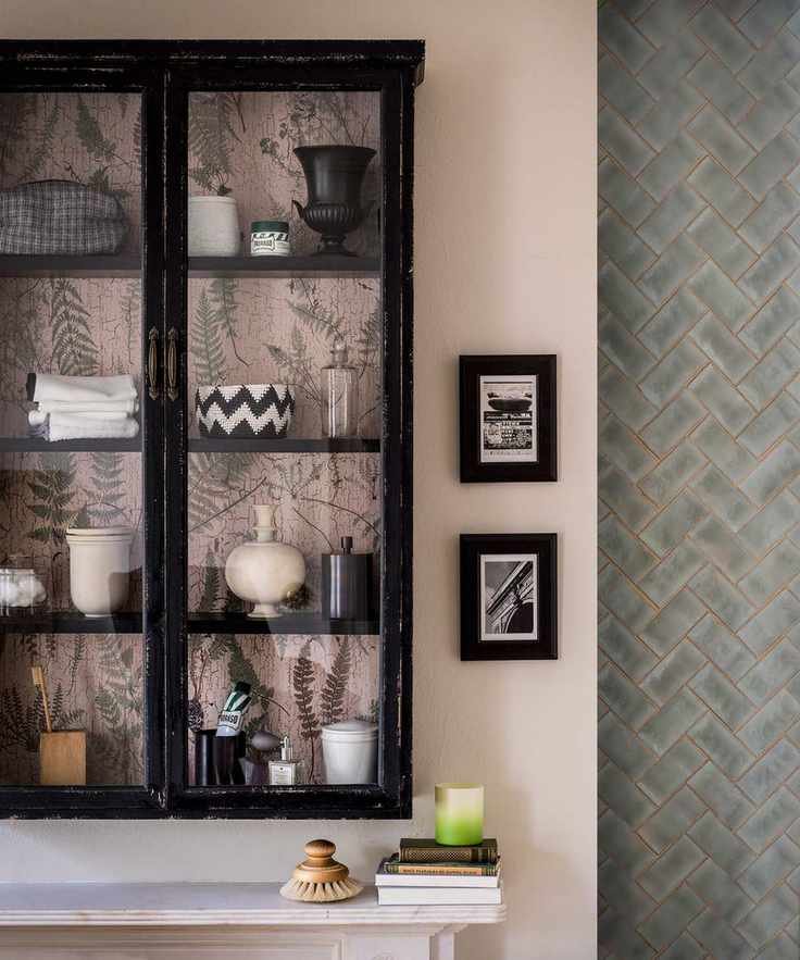 A glass-fronted bathroom storage cabinet containing decorative pots and towels