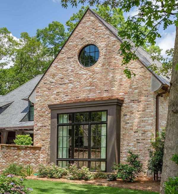 A red brick home exterior with dark brown window trim and a small circular mirror on the upper floor.