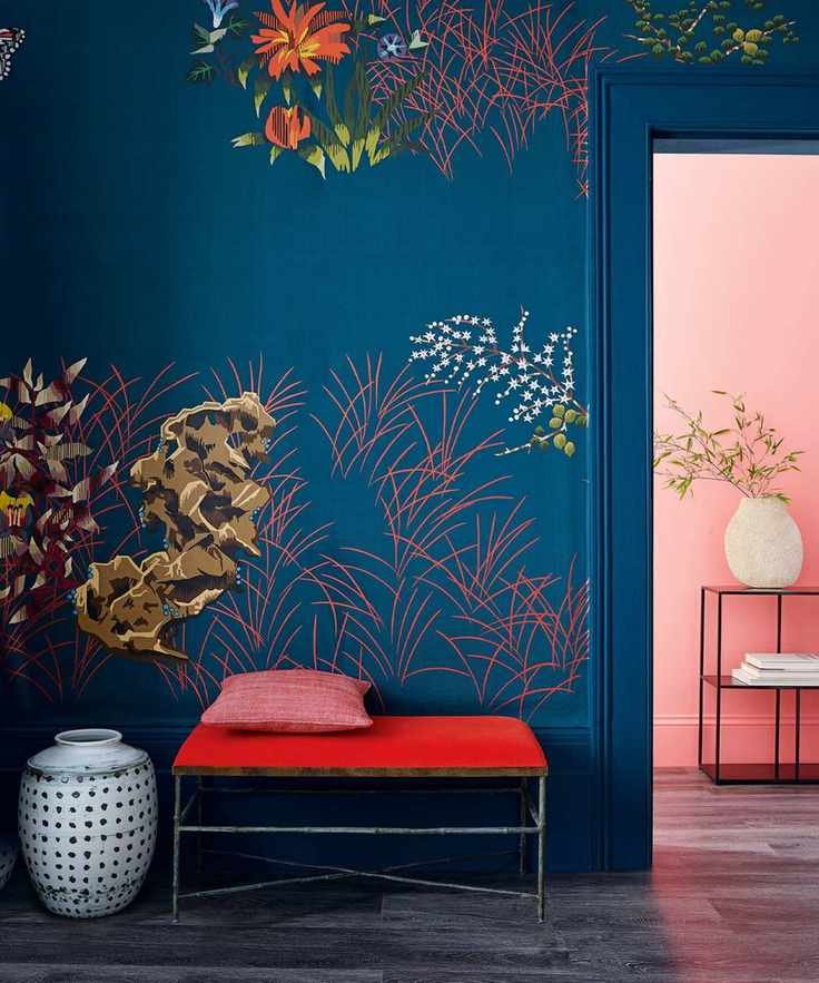 Hallway with bold, patterned dark blue wallpaper with contemporary floral patterns, dark black flooring, red bench with black metal frame, black and white spotted vase next to bench, looking out to corridor painted pink