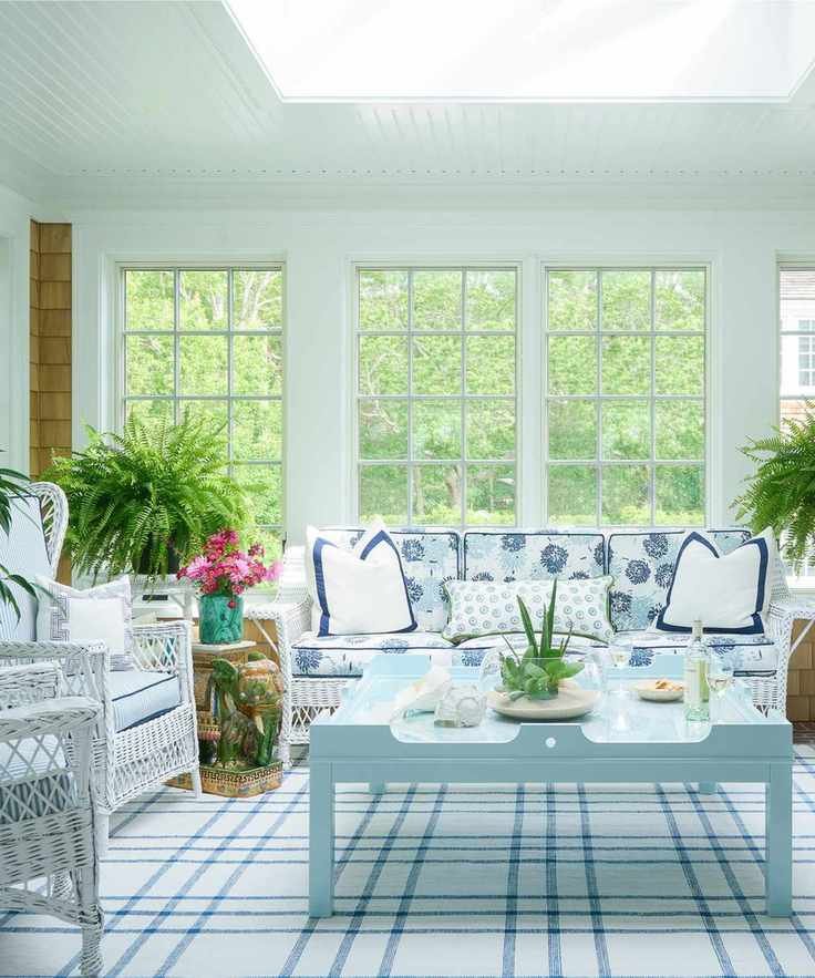 A coastal living room with wicker furniture, large windows and a vintage couch