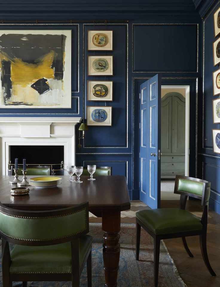 A dining room painted blue with antique artwork, a wooden table, and green dining chairs