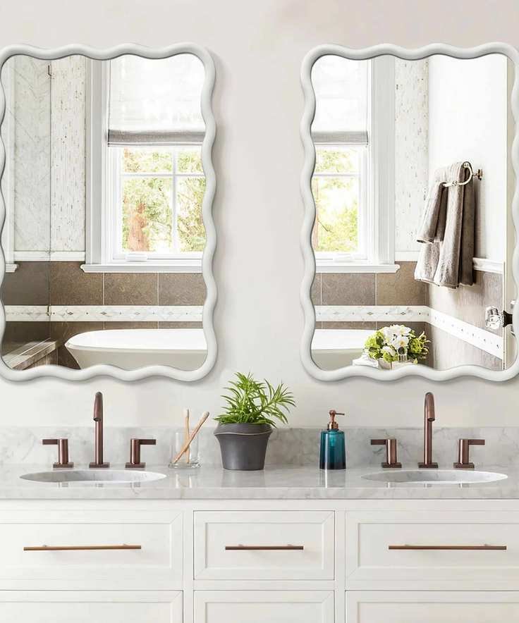 A white bathroom with wavy vanity mirrors and bronze faucets