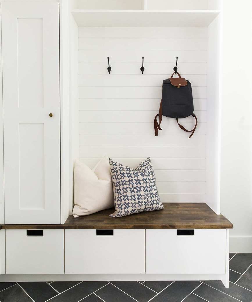 A white mudroom with a boot bench, drawers for shoes, and black wall hooks