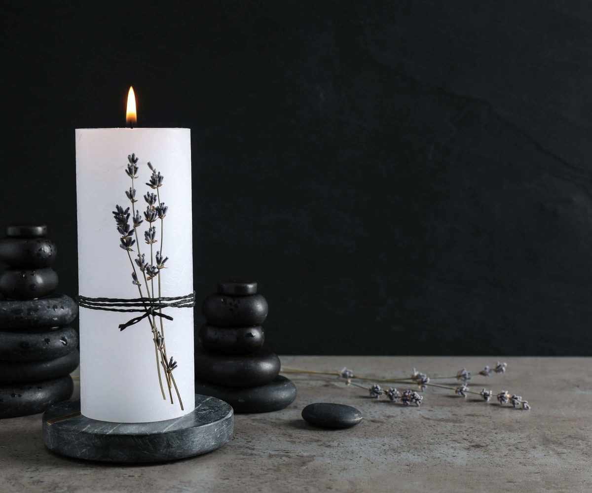 A single candle with lavendar wrapped around it and smooth dark stones