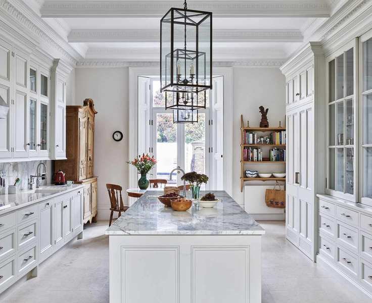 A kitchen with white cabinets and a marble topped island, with natural stone kitchen floor tile ideas.