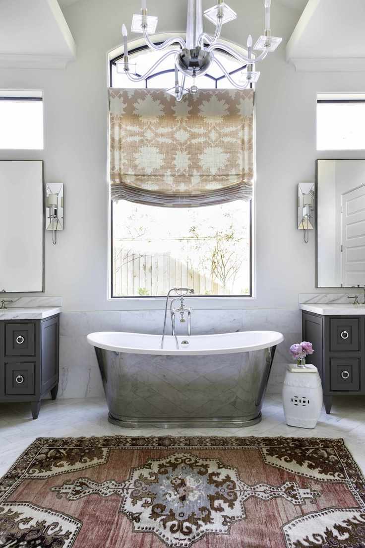 Silver bath with large window and twin grey sinks either side and warm coloured rug and curtain